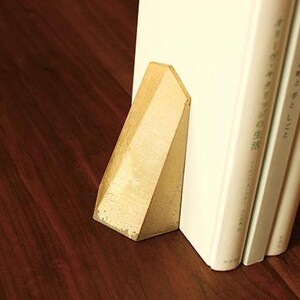 May include: A gold metal bookend with a triangular shape. The bookend is holding up three white books with Japanese text on the spines.