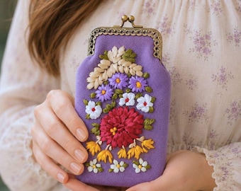 May include: A lavender fabric coin purse with a bronze-toned metal kiss-lock clasp. The front features intricate floral embroidery in shades of red, yellow, white, and purple, depicting a bouquet of various small flowers and leaves.