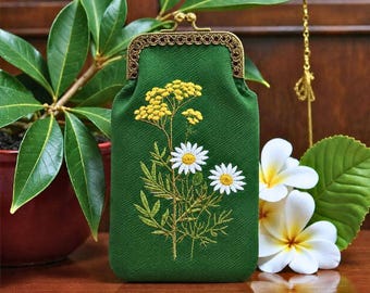 May include: A rectangular green fabric pouch featuring an embroidered design of yellow yarrow and white daisy flowers. The pouch has a metallic bronze-coloured kiss-lock clasp with a decorative filigree pattern along the top edge.