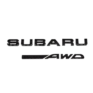Puede incluir: Emblemas negros de Subaru y AWD. El texto de Subaru está en negrita, sin serifa. El emblema AWD está en una fuente similar, con un diseño elegante y moderno. Los emblemas tienen un acabado brillante y probablemente están hechos de un material duradero.