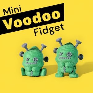 Puede incluir: Dos juguetes fidget de muñeco vudú verde con alfileres grises y ojos de botón sobre un fondo amarillo. El texto "Mini Voodoo Fidget" está en amarillo y negro.