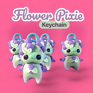 Könnte beinhalten: Eine Gruppe von Flower Pixie-Schlüsselanhängern vor einem pinkfarbenen Hintergrund. Jeder Schlüsselanhänger hat eine hellgrüne Figur mit lila und weißen floralen Details, blauen Augen und einer passenden blauen Schlaufe. Der Text "Flower Pixie Keychain" ist oben zu sehen.