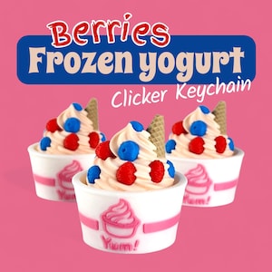 Op de afbeelding: Drie sleutelhangers met bevroren yoghurt op een roze achtergrond. Elke sleutelhanger toont een werveling van softijs, gegarneerd met rode frambozen, blauwe bosbessen en een wafel. De witte bekers hebben een roze wervelontwerp en het woord "Yum!"