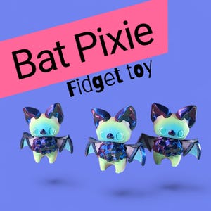 May include: Three iridescent bat-shaped fidget toys with large ears and wings are displayed against a blue background. The toys have a light green body and a dark, shiny chest. The text "Bat Pixie Fidget toy" is displayed in the image.