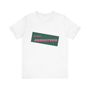 May include: White t-shirt with a green rectangle and the text "but first, sunscreen" in pink.