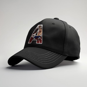May include: Black baseball cap with a curved brim and a stitched design. The cap features a colorful graphic of a character inside a white and red letter "A". The cap is a stylish accessory.