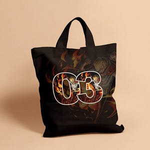 May include: Black tote bag featuring a graphic of a character with blonde hair and the number "03" in a fiery design. The background shows a fiery scene with other characters. The bag has black handles.
