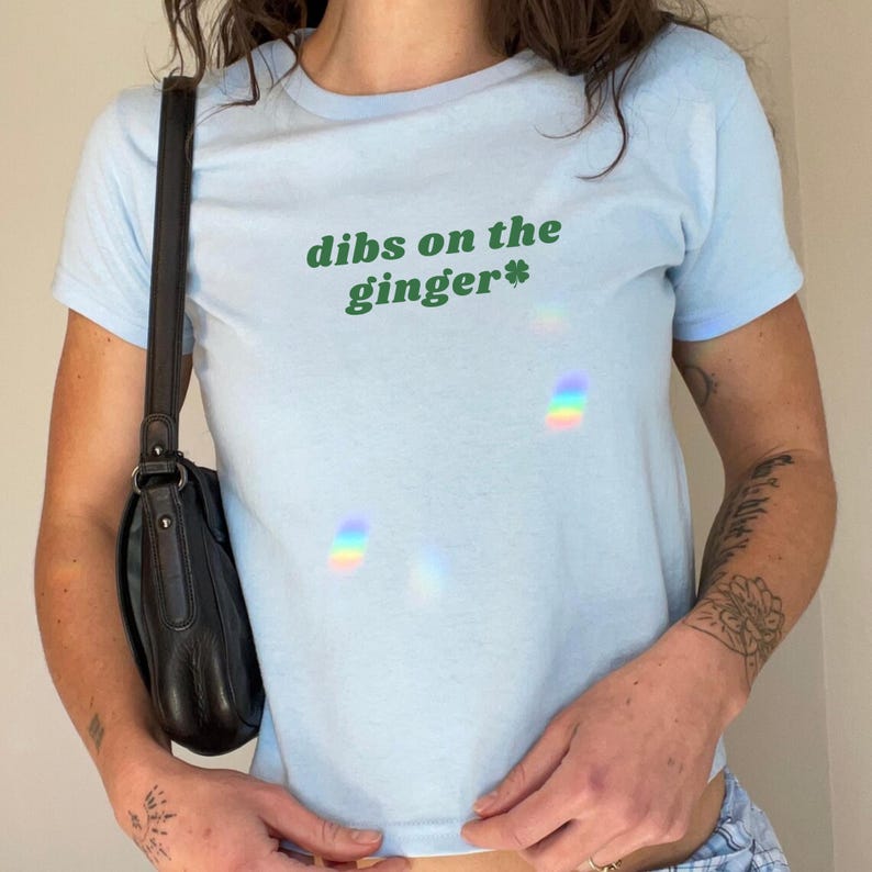 Puede incluir: Una camiseta azul claro con el texto "dibs on the ginger*" impreso en verde.