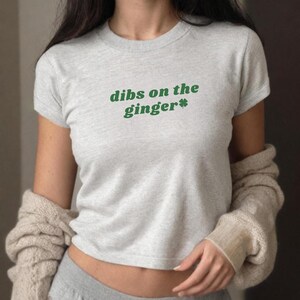 Puede incluir: Una camiseta gris de manga corta con el texto "dibs on the ginger*" en letras verdes. Un tr&eacute;bol de cuatro hojas verde est&aacute; al lado de la palabra "ginger".