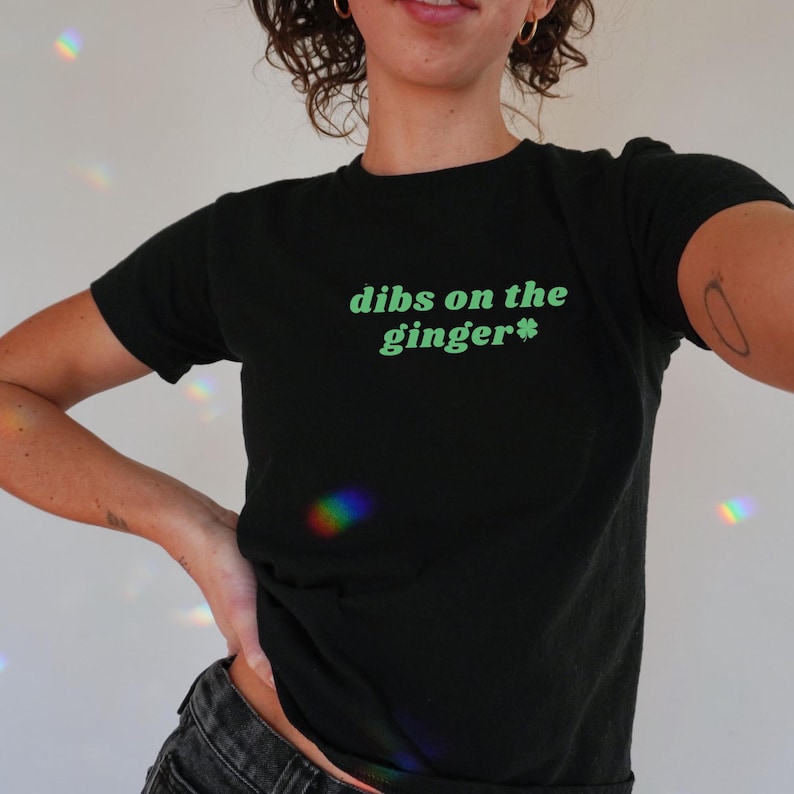 Puede incluir: Camiseta negra con texto verde que dice "dibs on the ginger*" con un tr&eacute;bol verde.