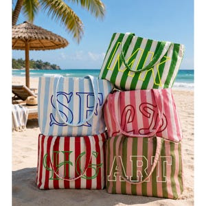 Puede incluir: Una colección de cuatro bolsos tote rectangulares de lona con rayas verticales en verde, azul claro, rosa y rojo. Cada bolso presenta grandes letras de monograma bordadas en colores contrastantes, incluyendo MK, SF, LD, HG y ART, con dos correas.