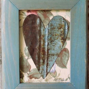 May include: A framed piece of art featuring a rusty metal heart shape on a floral fabric background. The frame is a light blue color with a distressed finish. The text "believe in yourself" is printed on a small white tag below the heart.