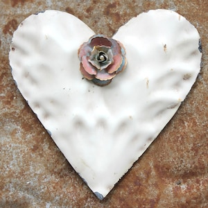 May include: White metal heart-shaped ornament with a pink and blue metal flower in the center.