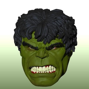 May include: A sculpted head of a green-skinned character with thick, dark, textured hair. The face features a furrowed brow, intense eyes, and a wide, aggressive expression with bared white teeth and visible gums, rendered in a 3D digital style.