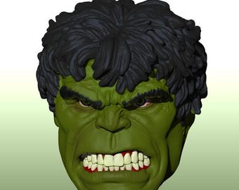 以下が含まれることがあります： 緑色の肌をしたキャラクターの彫刻された頭部で、厚みのある暗い質感の髪をしています。顔にはしわの寄った額、鋭い目つき、そして白い歯と歯茎が見える大きく攻撃的な表情が表現されており、3Dデジタルスタイルで描かれています。