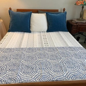 May include: A white bed with a blue and white patterned duvet cover. The bed has two blue pillows and one white pillow with a geometric pattern.