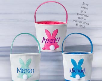 May include: Three white Easter baskets with bunny ears and personalized names. The baskets are pink, blue, and green. The text on the baskets reads "Avery", "Mateo", and "Michael".