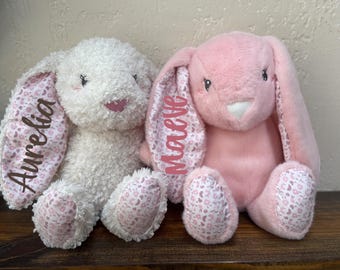 May include: Two plush bunny toys with pink and white floral fabric ears. The white bunny has the name "Aurelia" embroidered on one ear and the pink bunny has the name "Marcelle" embroidered on one ear.
