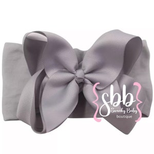 May include: A gray headband with a large gray bow. The headband is made of soft, stretchy fabric and is perfect for babies and toddlers. The bow is made of satin ribbon and is tied in a classic bow shape. The headband is adorned with the text "Swanky Baby Boutique".