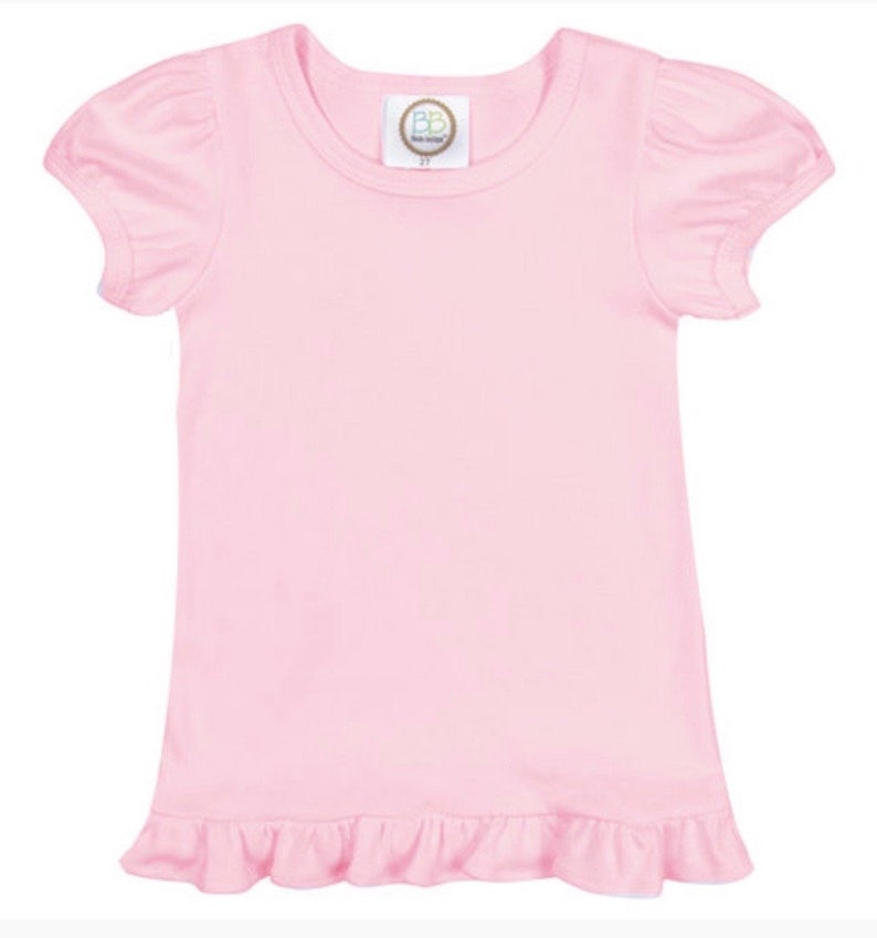 K&ouml;nnte beinhalten: Hellrosa kurz&auml;rmeliges Shirt mit Rundhalsausschnitt und R&uuml;schensaum. Die &Auml;rmel sind gepufft. Ein kleines Etikett mit dem Text "BB" und der Zahl "2T" ist am Ausschnitt sichtbar.