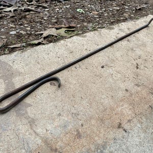 May include: A rusty metal hook with a long handle. The hook is bent at the end to form a loop.