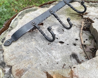 May include: A black metal wall-mounted hook rack with three twisted hooks. The rack is mounted on a wooden surface.