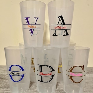 Può includere: Una collezione di bicchieri di plastica trasparenti, ciascuno personalizzato con un nome e un'iniziale. I nomi includono Victor, Alicia, Olivia, Daniel e Christine. Le iniziali e i nomi sono in vari colori, tra cui viola, nero, blu e marrone.