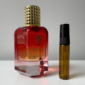 May include: A perfume bottle with a red and gold gradient, a gold cap, and a smaller brown spray bottle. The perfume bottle has the text "d'LIMAR Elixir d'Amour" on the front. The smaller bottle has a black cap.