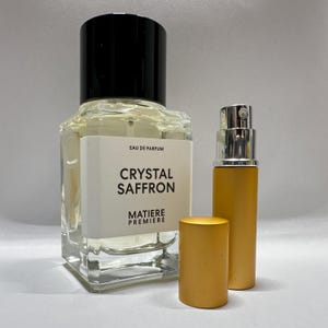 May include: A clear glass perfume bottle with a black cap and a smaller, gold-colored travel-size spray bottle. The label on the larger bottle reads "Crystal Saffron" and "Matiere Premiere."