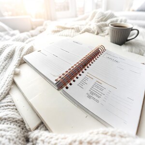 May include: A white spiral bound planner with a copper coil. The planner has a section for daily to-do lists and a section for weekly goals. The planner is open to a page with a list of daily prayers.