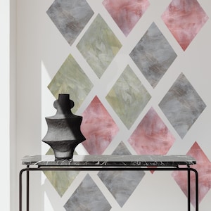May include: A black sculptural vase with a textured surface sits on a rectangular black marble console table with thin metal legs. Behind the table, the wall features a repeating pattern of diamond-shaped decals in shades of grey, pink, and olive green.