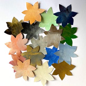 Puede incluir: Una colección de recortes de papel con forma de flor de colores. Los pétalos están pintados en varios tonos, incluyendo naranja, verde, azul y dorado. El papel tiene un aspecto texturizado, con pinceladas visibles.