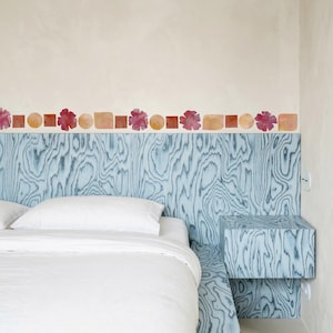 Pode incluir: Quarto com cabeceira e mesa de cabeceira a condizer com grão de madeira azul. A cabeceira tem uma borda decorativa de formas em aquarela em vermelho, laranja e bege. A cama tem roupa de cama branca.