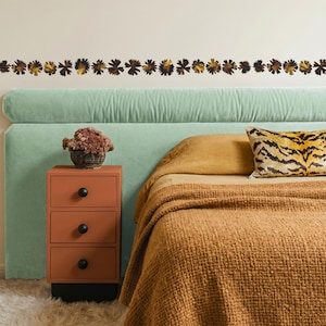 May include: A bedroom scene featuring a bed with a light green headboard, a rust-colored nightstand with black knobs, and a bedspread in shades of brown and gold. A decorative floral border adorns the wall above the headboard. A tiger-striped pillow adds a contrasting pattern.