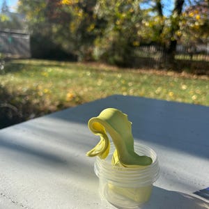 May include: A yellow slime in a clear plastic container. The slime is in a swirl shape and is sitting on a white table.