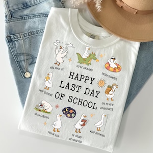 May include: White t-shirt with a graphic design featuring cartoon ducks and the text "HAPPY LAST DAY OF SCHOOL." The shirt includes phrases like "You Made It!" and "Enjoy Summer."