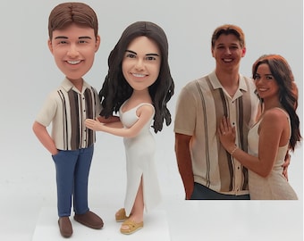 May include: A bobblehead figurine of a couple, the man in a short-sleeved shirt and blue pants, the woman in a white dress. A photo of a couple is in the background. The figurine is on a white base.