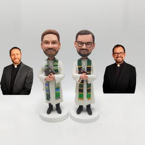 Può includere: Due statuette di preti, ognuna con un libro, su basi bianche. Indossano vesti bianche, stole a righe verdi e blu e scarpe nere. Due uomini in giacca e cravatta sono su entrambi i lati.