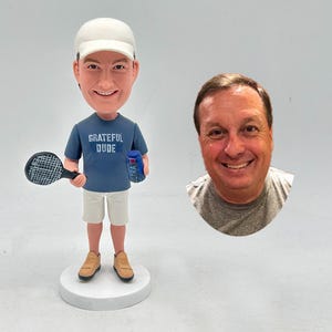 Könnte beinhalten: Figur einer Person in Tennisbekleidung, die einen Schläger und eine Bierdose hält. Die Figur trägt eine weiße Kappe, ein blaues T-Shirt mit dem Text "Grateful Dude", weiße Shorts und braune Turnschuhe. Daneben ein Foto eines lächelnden Mannes.