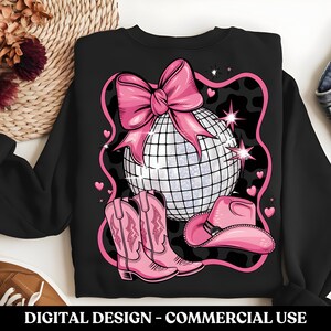 May include: Black sweatshirt featuring a pink bow, disco ball, cowboy hat, and boots. The design is on a black background with a white and black leopard print.