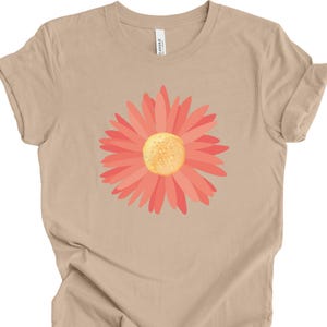 Puede incluir: Una camiseta beige con un estampado gr&aacute;fico de margarita rosa.