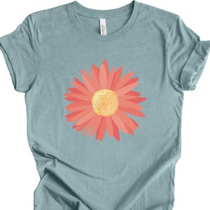 Puede incluir: Una camiseta azul claro con un gr&aacute;fico de margarita rosa.