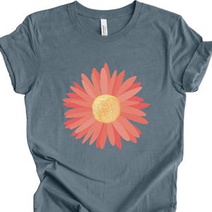 Puede incluir: Una camiseta azul con un gr&aacute;fico de flor de margarita de color coral.