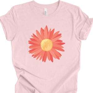 Puede incluir: Una camiseta rosa con un gr&aacute;fico de margarita de color coral.