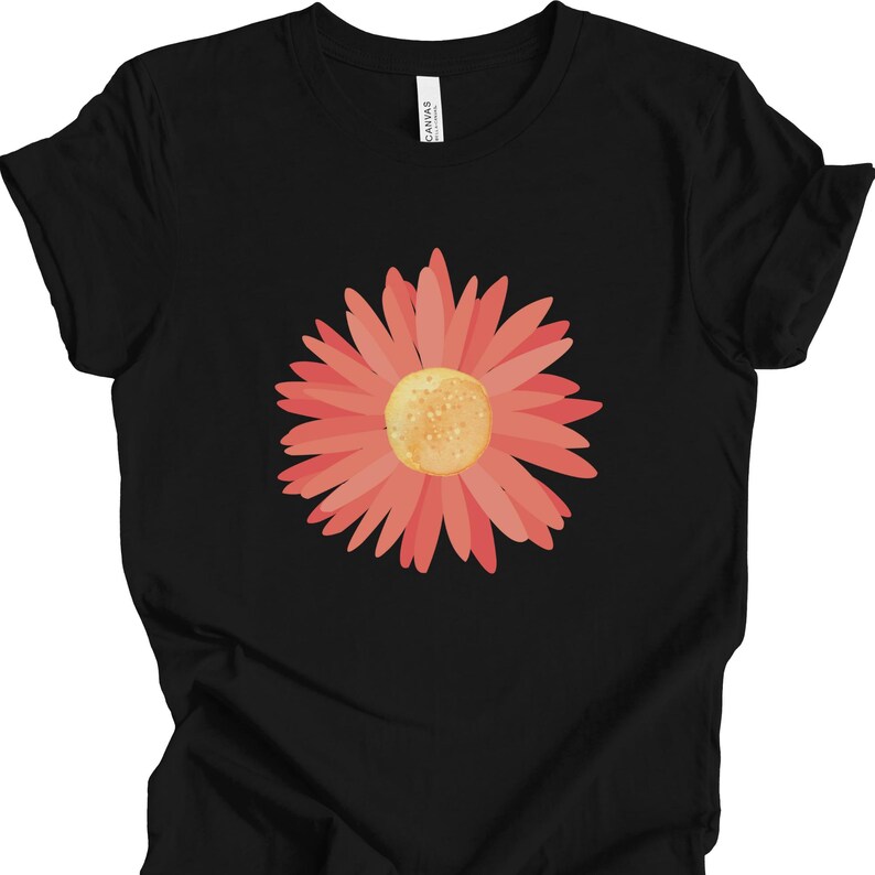 Puede incluir: Una camiseta negra con un gr&aacute;fico de flor rosa. La flor tiene un centro amarillo y est&aacute; en el centro de la camiseta.