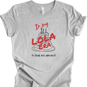 May include: A gray t-shirt with a black and red graphic of a birthday cake with candles and the text "In my Lola Era Is that not allowed?!"