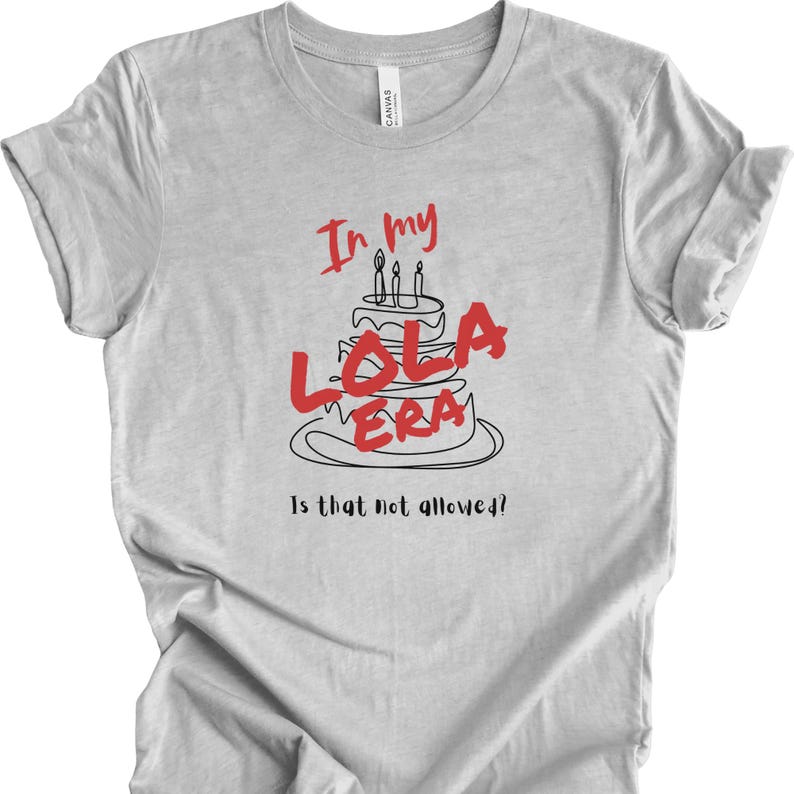 May include: A gray t-shirt with a black and red graphic of a birthday cake with candles and the text "In my Lola Era Is that not allowed?!"