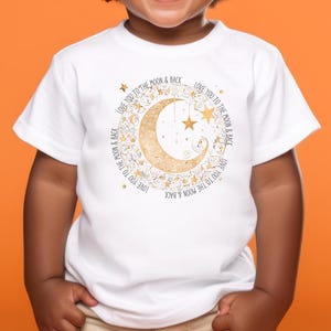 Puede incluir: Camiseta blanca para niño pequeño con un gráfico de media luna dorada y estrellas. El texto "Love you to the moon & back" se repite alrededor de la luna.