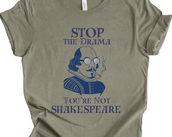 May include: Olive green t-shirt with a blue graphic of William Shakespeare wearing glasses and smoking a cigarette. The text "STOP THE DRAMA" and "YOU'RE NOT SHAKESPEARE" are printed in blue.