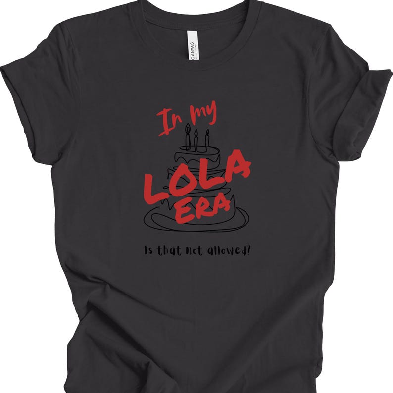 May include: A dark gray t-shirt with a black and white illustration of a birthday cake with the text "In my Lola Era" in red. The text "Is that not allowed?" is printed below the cake.